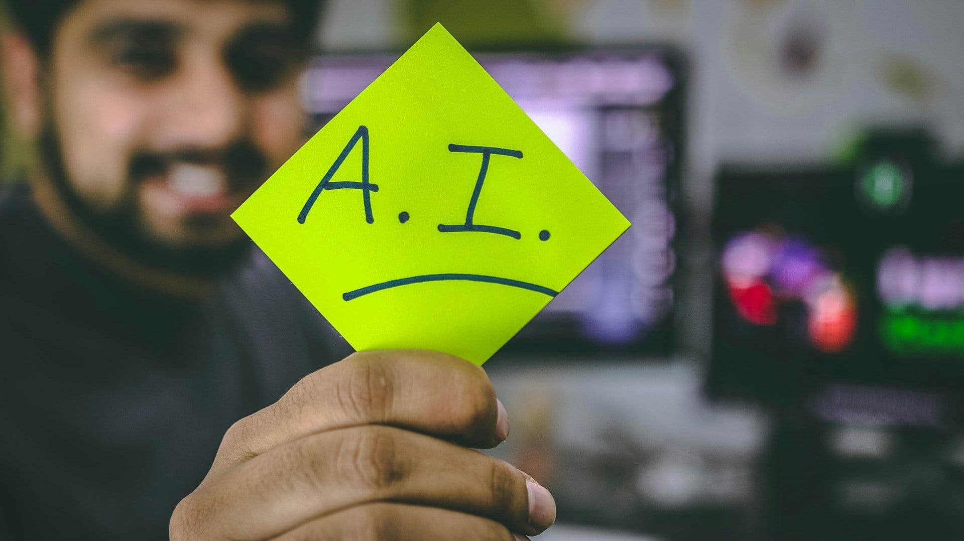 [syncsoft-auto][src:unsplash|id:1526378722484-bd91ca387e72] A person holding a sticky note labeled A.I. beside a developer monitor, illustrating the enterprise AI agent control plane and multi-agent orchestration trend of 2026