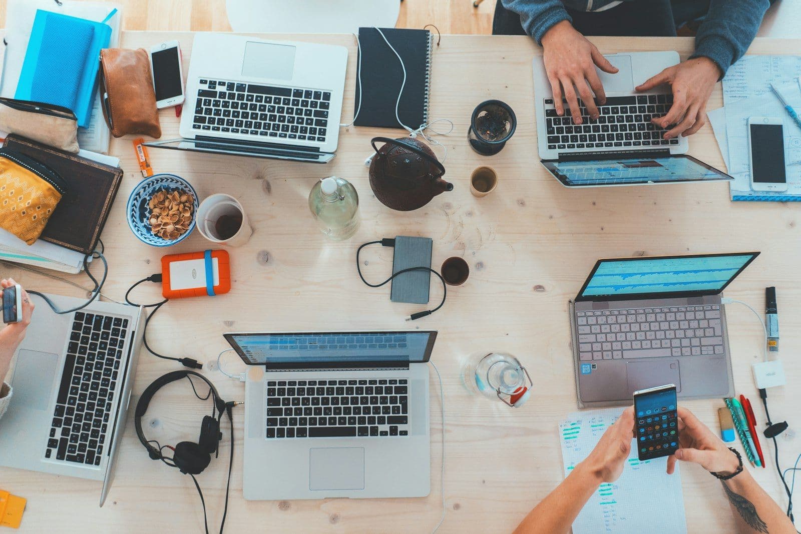 [syncsoft-auto][src:unsplash|id:1519389950473-47ba0277781c] Top-down view of a cross-functional team collaborating with laptops and devices — representing generative-AI BPO operations
